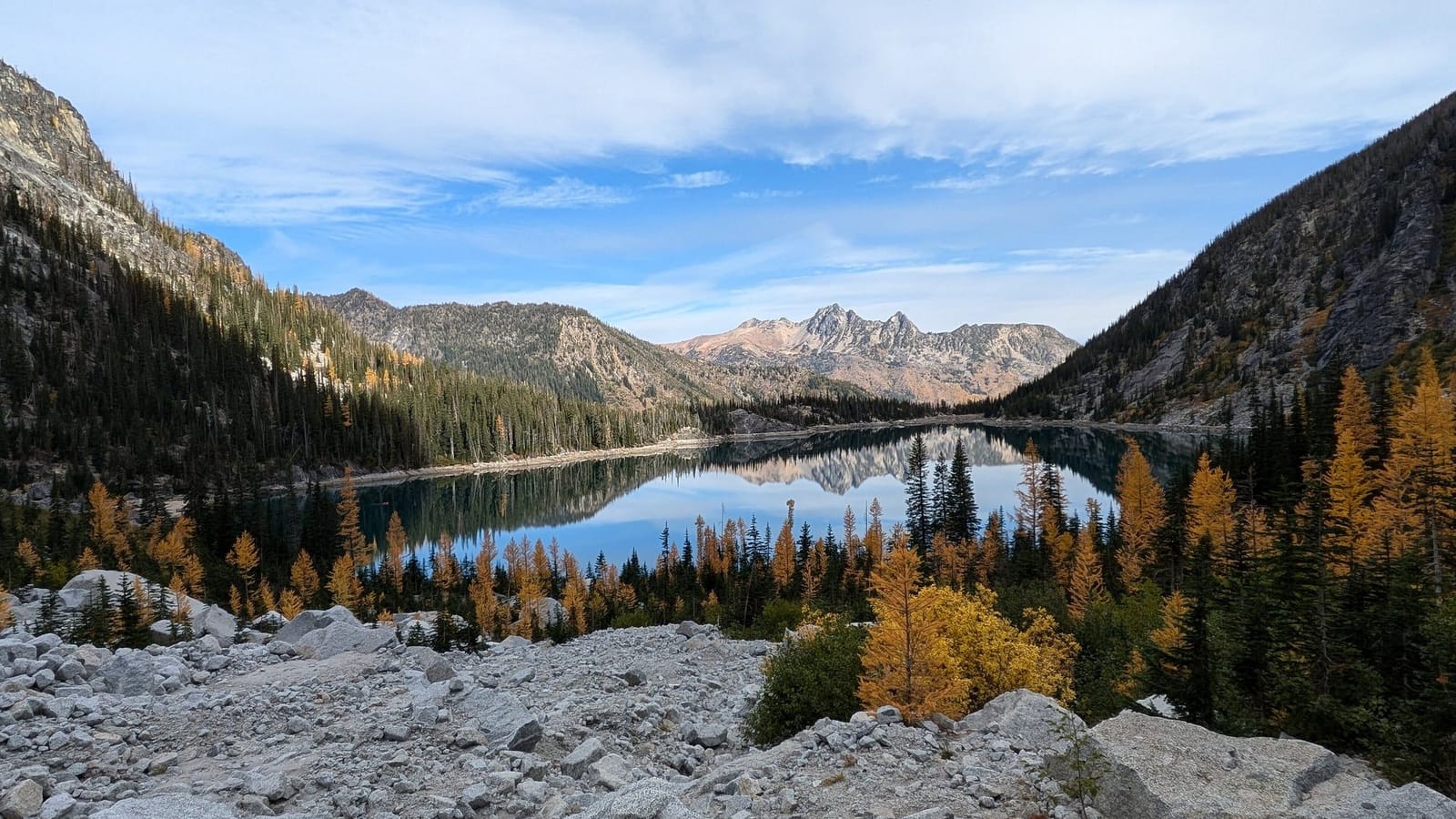 Colchuck Lake ringed by golden larches and granite boulders, with Enchantment peaks in the distance