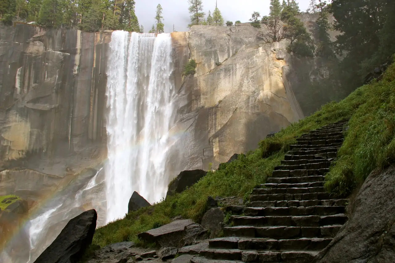 Granite steps of the Mist Trail climbing beside Vernal Fall, with a rainbow in the spray