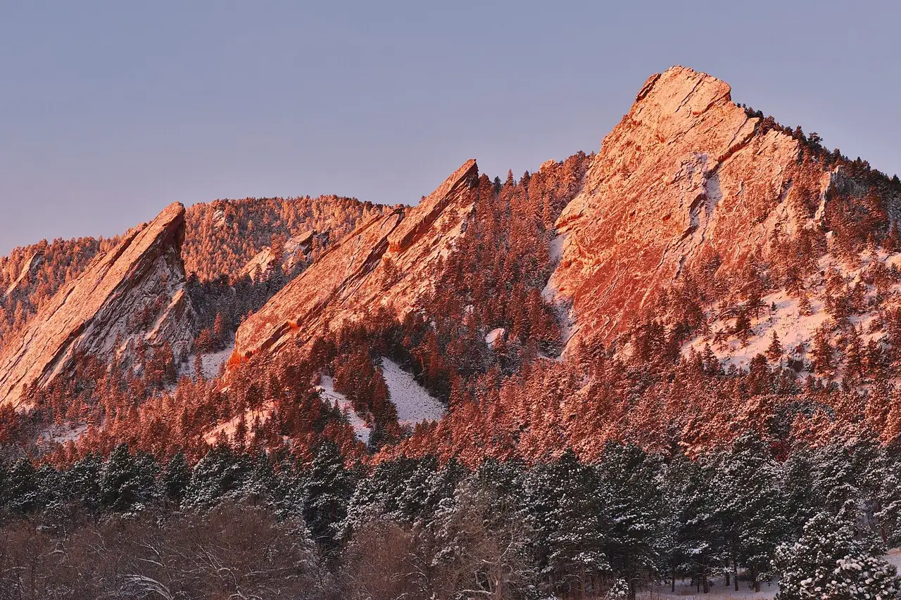The Flatirons glowing at sunrise above snowy Chautauqua meadow in February
