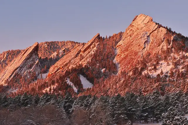 The Flatirons glowing at sunrise above snowy Chautauqua meadow in February