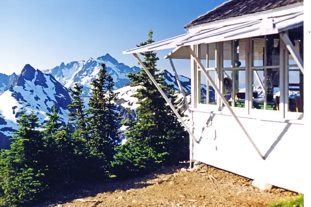 The Winchester Mountain lookout with snowy border peaks behind it in August