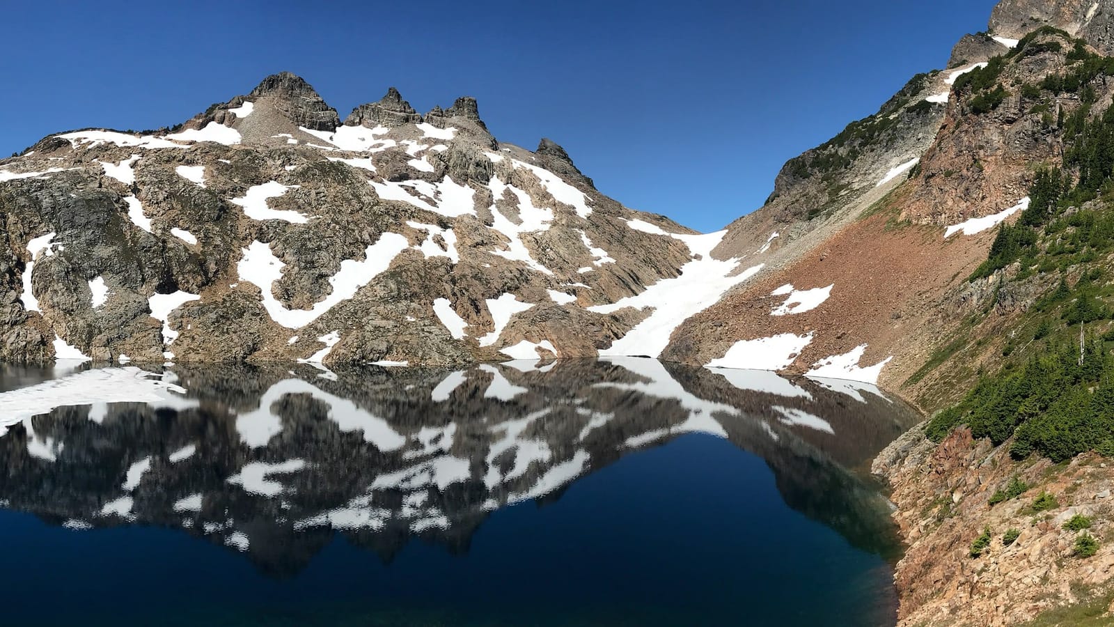 Snow-patched Gothic Peak reflected in the dark water of Foggy Lake in Gothic Basin