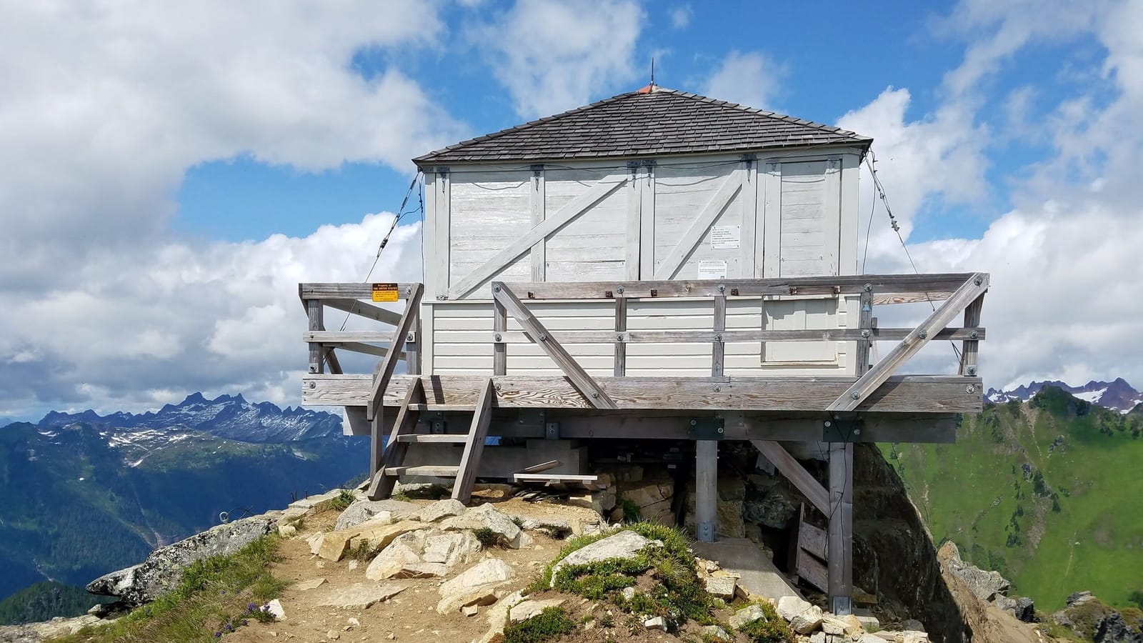 The Green Mountain fire lookout braced on its rocky summit, with cloud-capped Cascade peaks behind