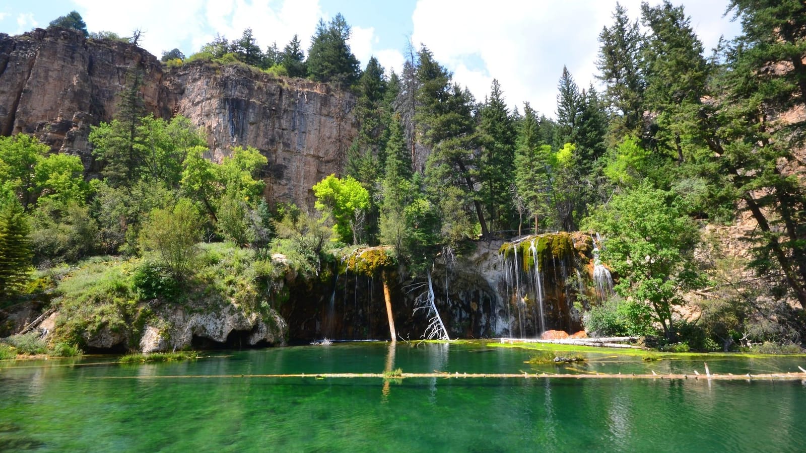 Emerald Hanging Lake with thin waterfalls spilling over its travertine rim
