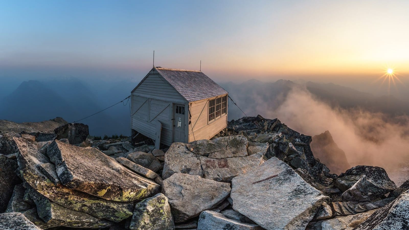 Hidden Lake Lookout cabin on a granite summit at sunset, with smoke haze filling the valleys