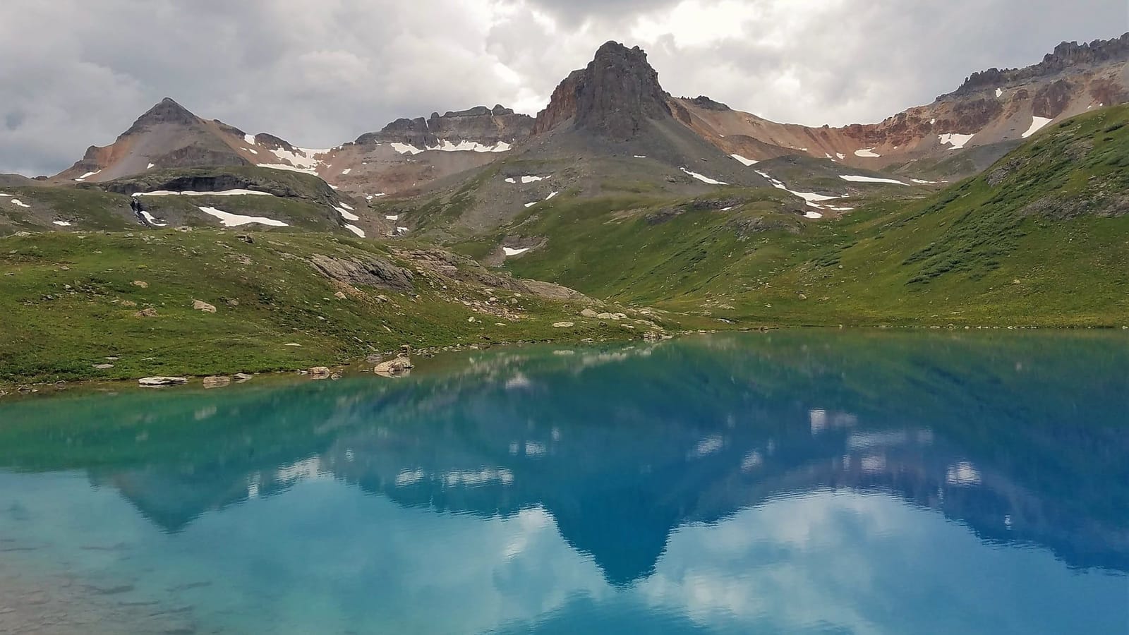 Turquoise Ice Lake reflecting clouds beneath the pointed summits of the San Juan Mountains