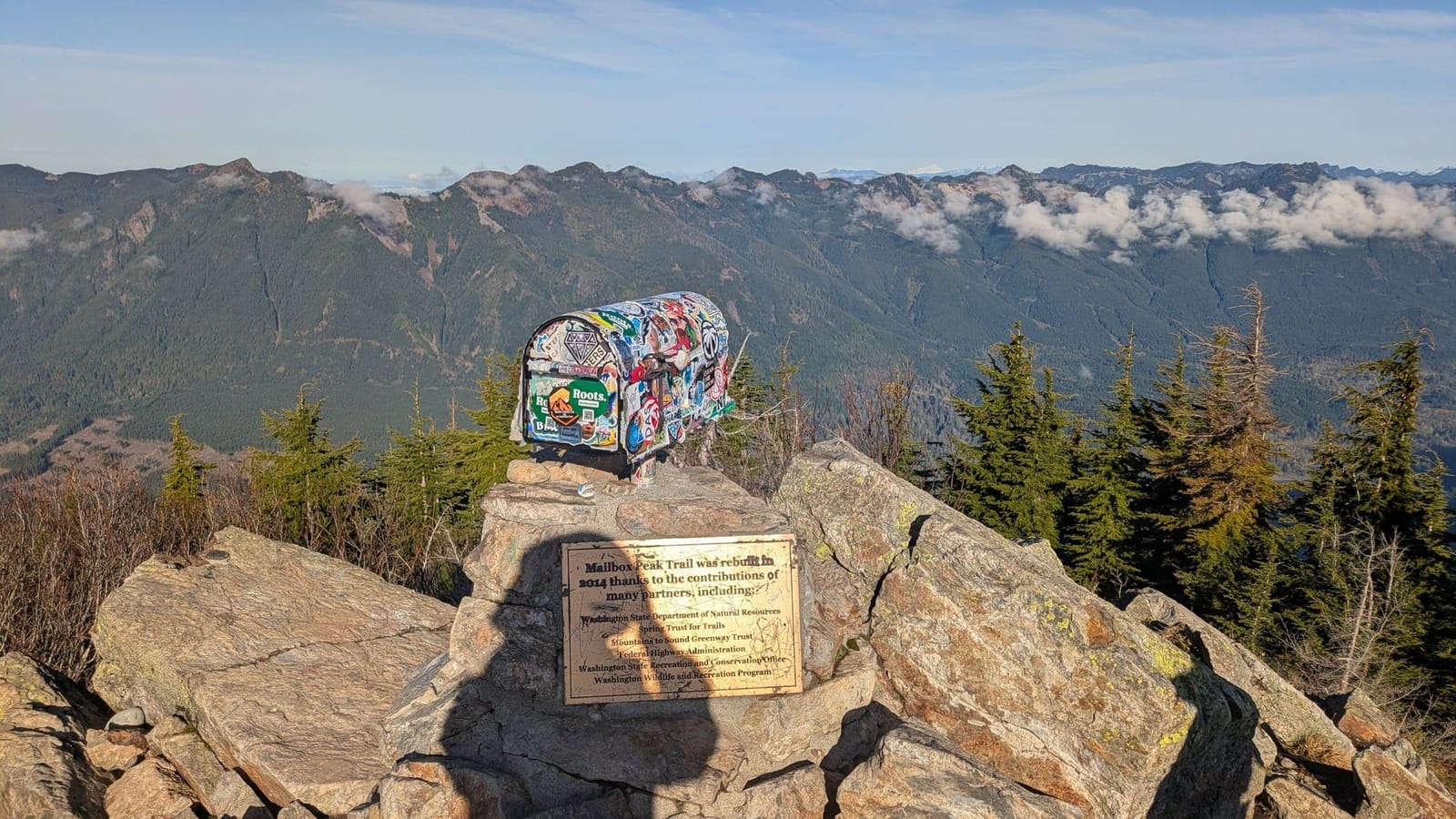 The sticker-covered mailbox bolted to the summit rocks of Mailbox Peak, with Cascade ridges behind