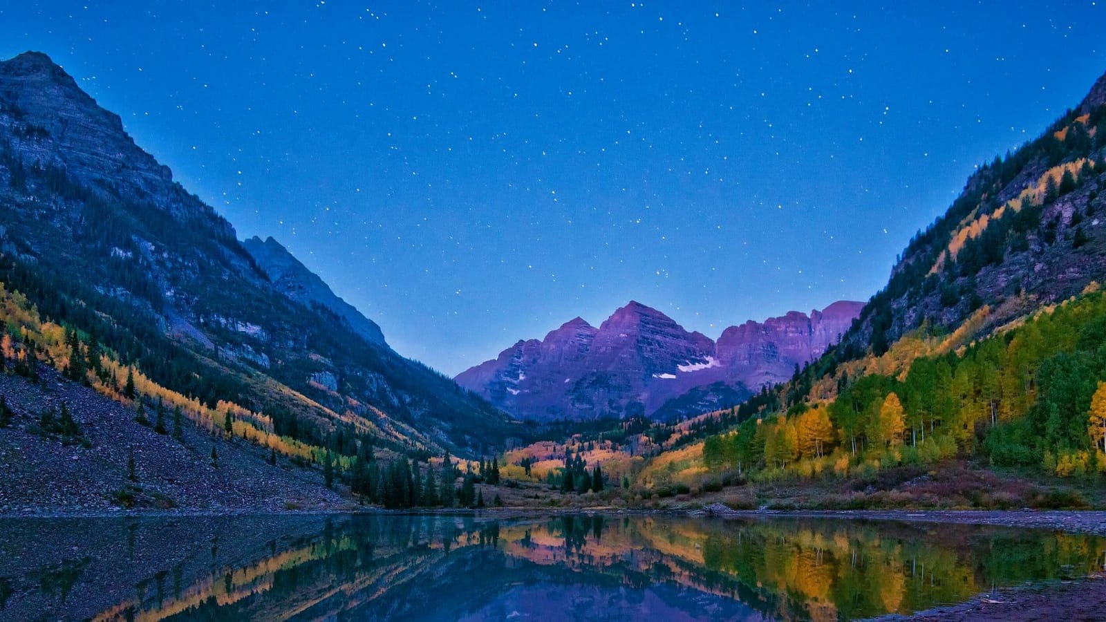 The Maroon Bells in pre-dawn alpenglow reflected in Maroon Lake, with golden aspens on the slopes