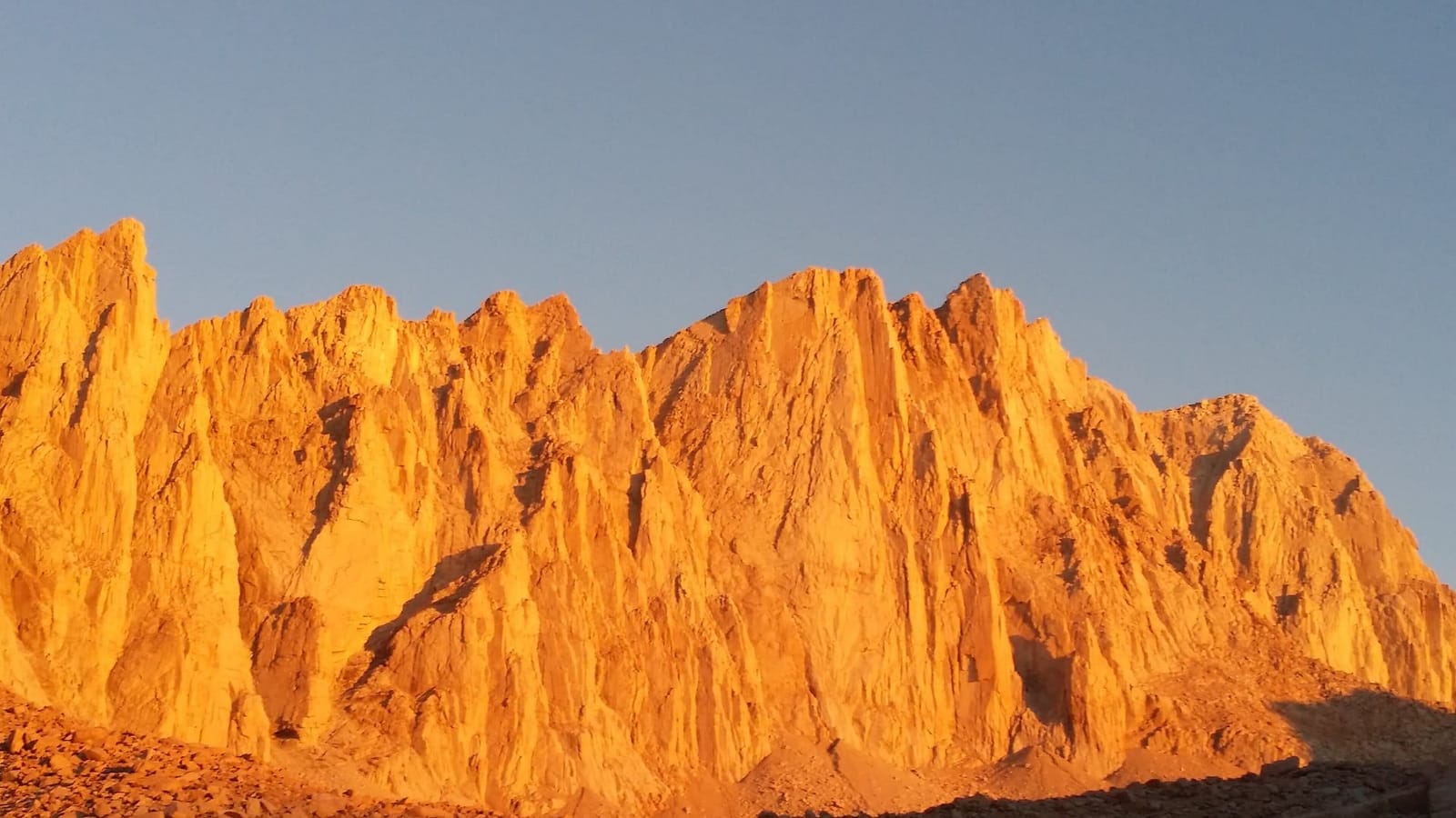 The east face of Mt. Whitney and its needles glowing orange at sunrise, seen from Trail Camp
