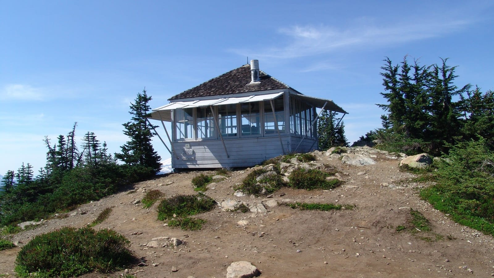 The white Winchester Mountain fire lookout on its bare summit, ringed by subalpine firs
